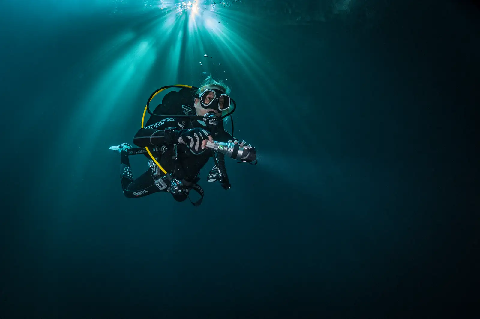 Diver with torch in dark deep water with sunbeams above
