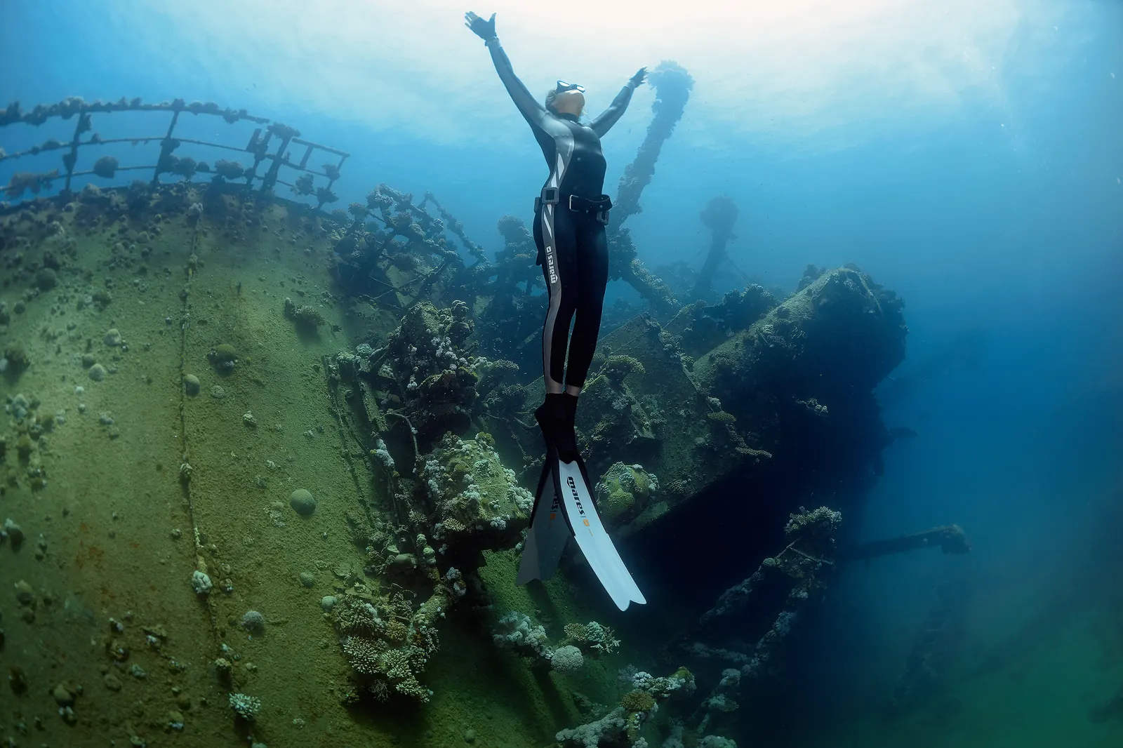 Diver ascending in front of a large sunken wreck structure