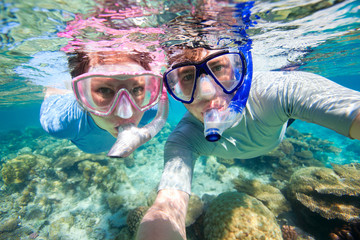 One male and one female snorkelling at havelock lighthouse while underwater corals and marine life is visible in crystal clear waters
