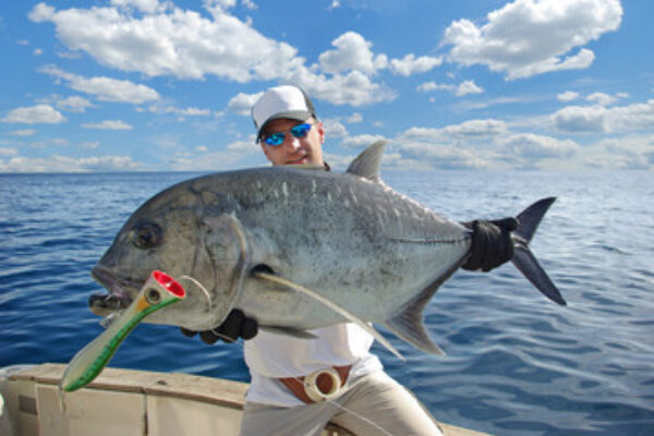 A man standing on a fishing boat in the sea and displaying a big fish 