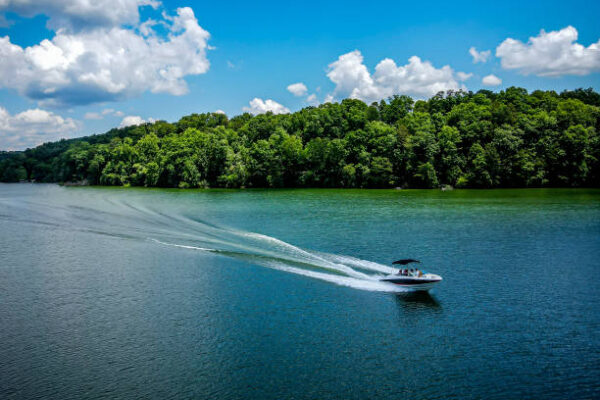 Speed boat ride on andaman sea with a trail of wake.  Green trees and white clouds in the sky.