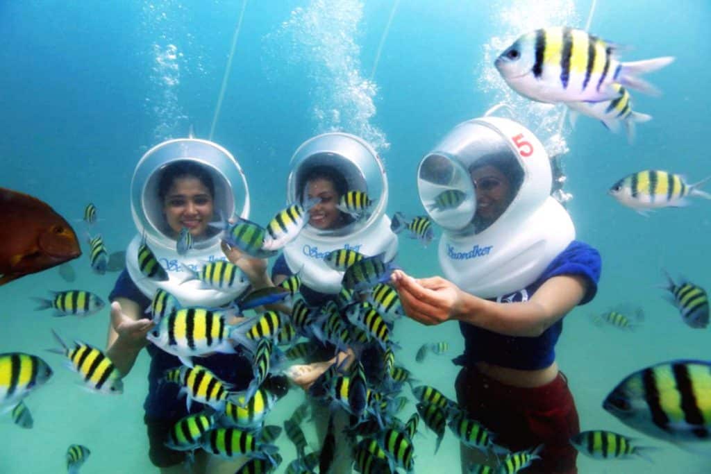 3 female guests doing sea walk underwater in andaman and interacting with multiple species of colorful fishes.