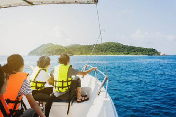 3 people on a speed boat venturing on the blue sea water and approaching to a virgin Island ahead.   